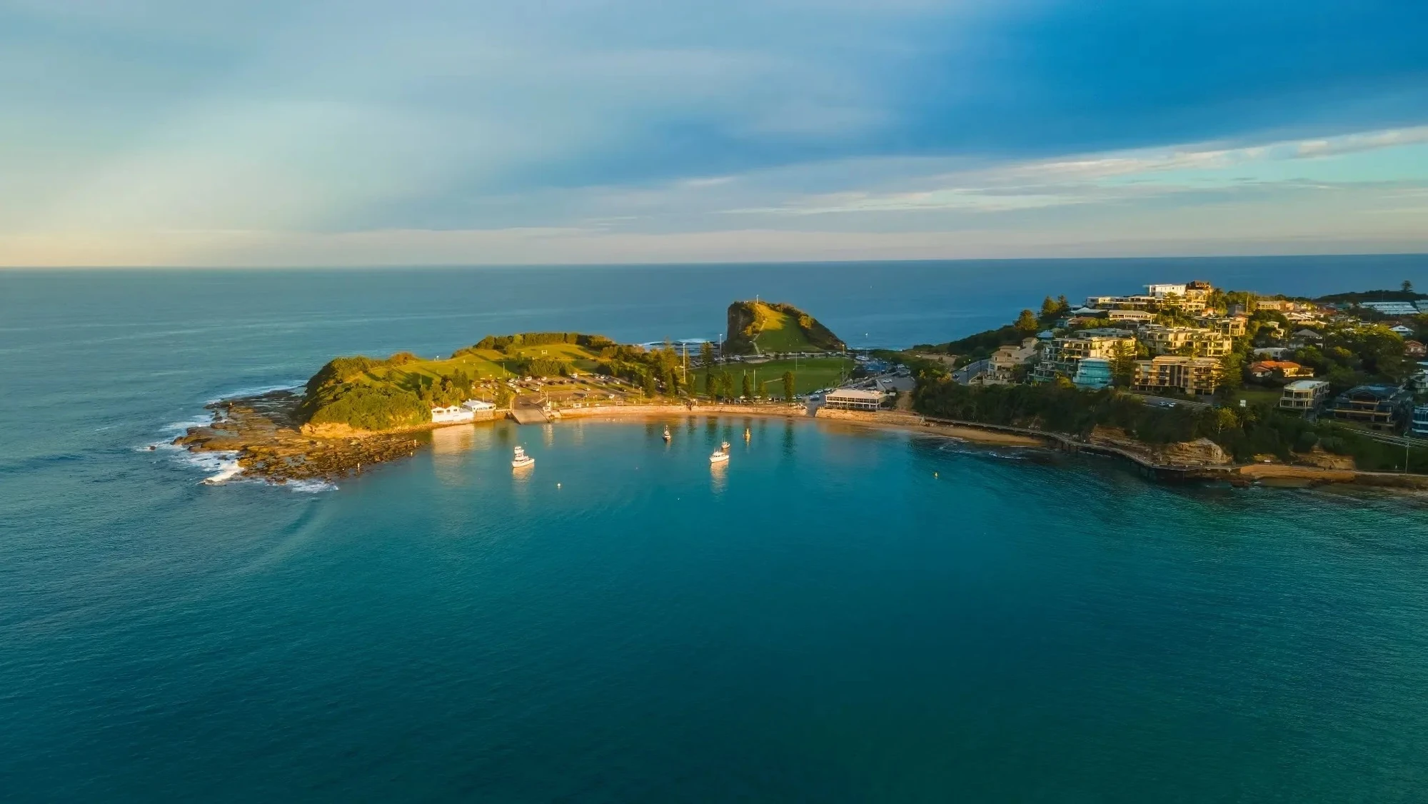 Aerial view of Terrigal and coastal headland with boats anchored in calm turquoise water at golden hour