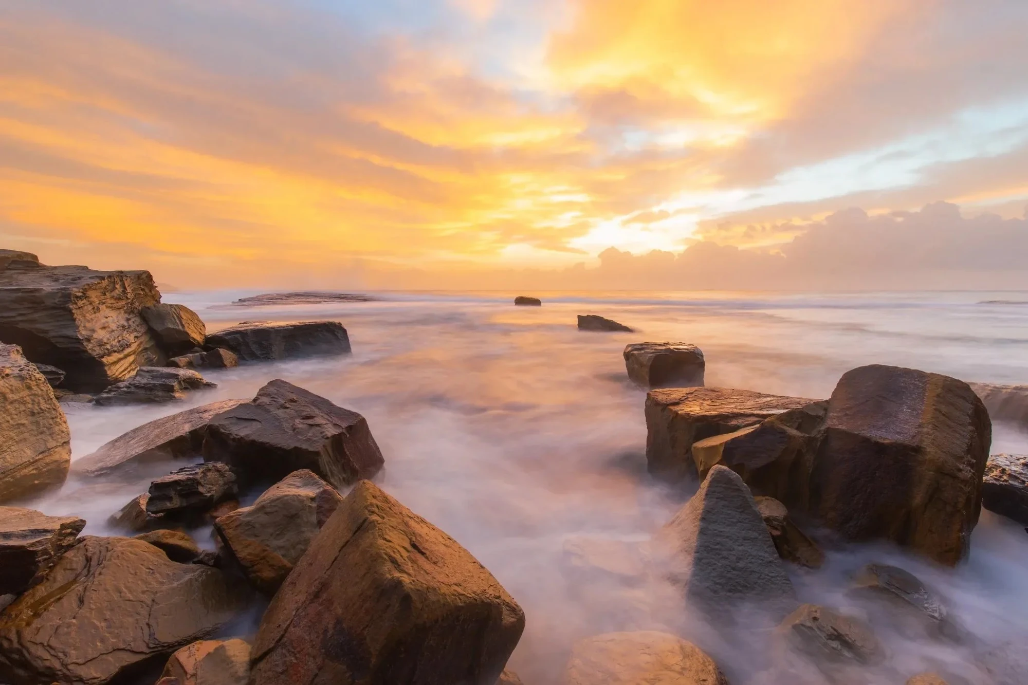 Sunrise over ocean rocks on the Central Coast, waves flowing gently around the stone platforms